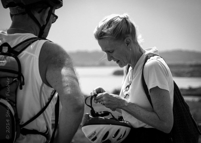 Older woman getting ready to put on her bike helmet as her male bicyling partner waits and watches.