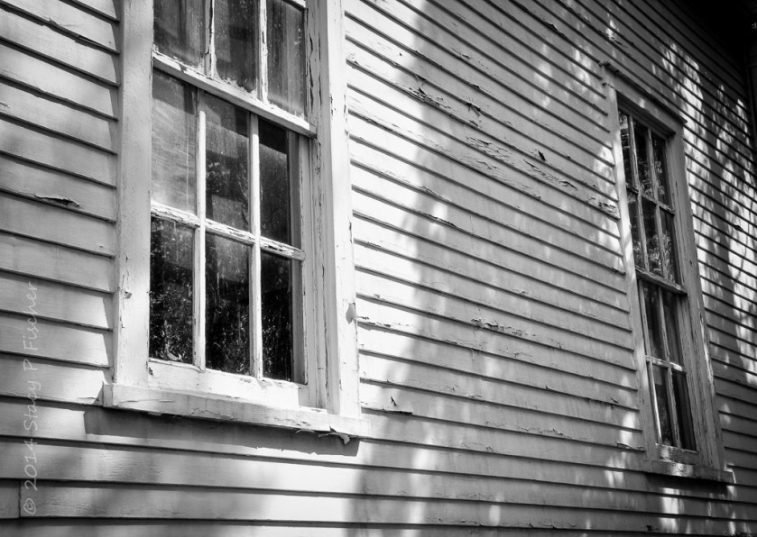 Weathered clapboards with peeling paint and two paned windows.