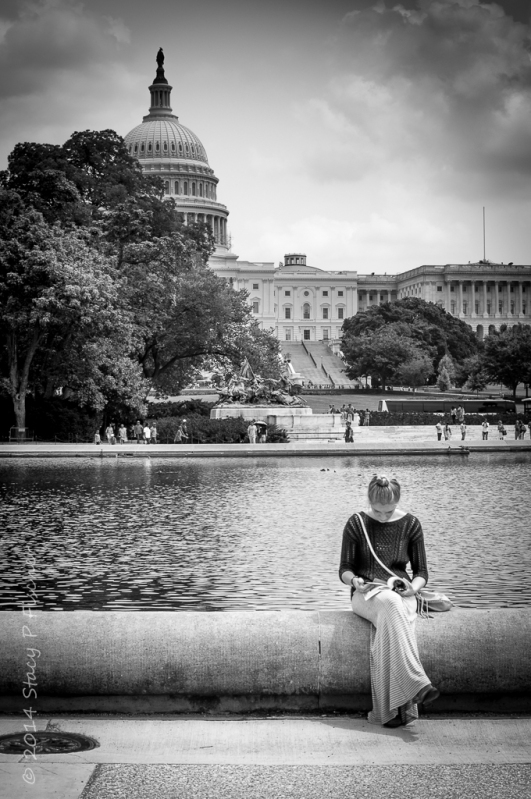 Woman sitting on the edge of the pool, reading, with US Capitol in the background.