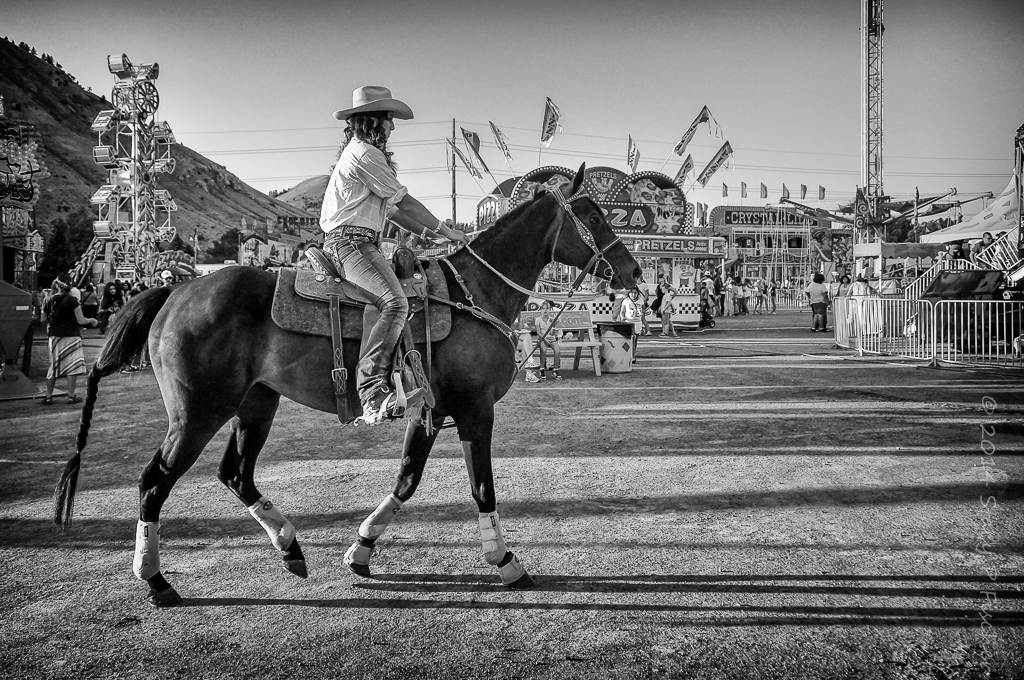 Rodeo cowgirl on horse heading to the arena, against the backdrop of the county fair rides.