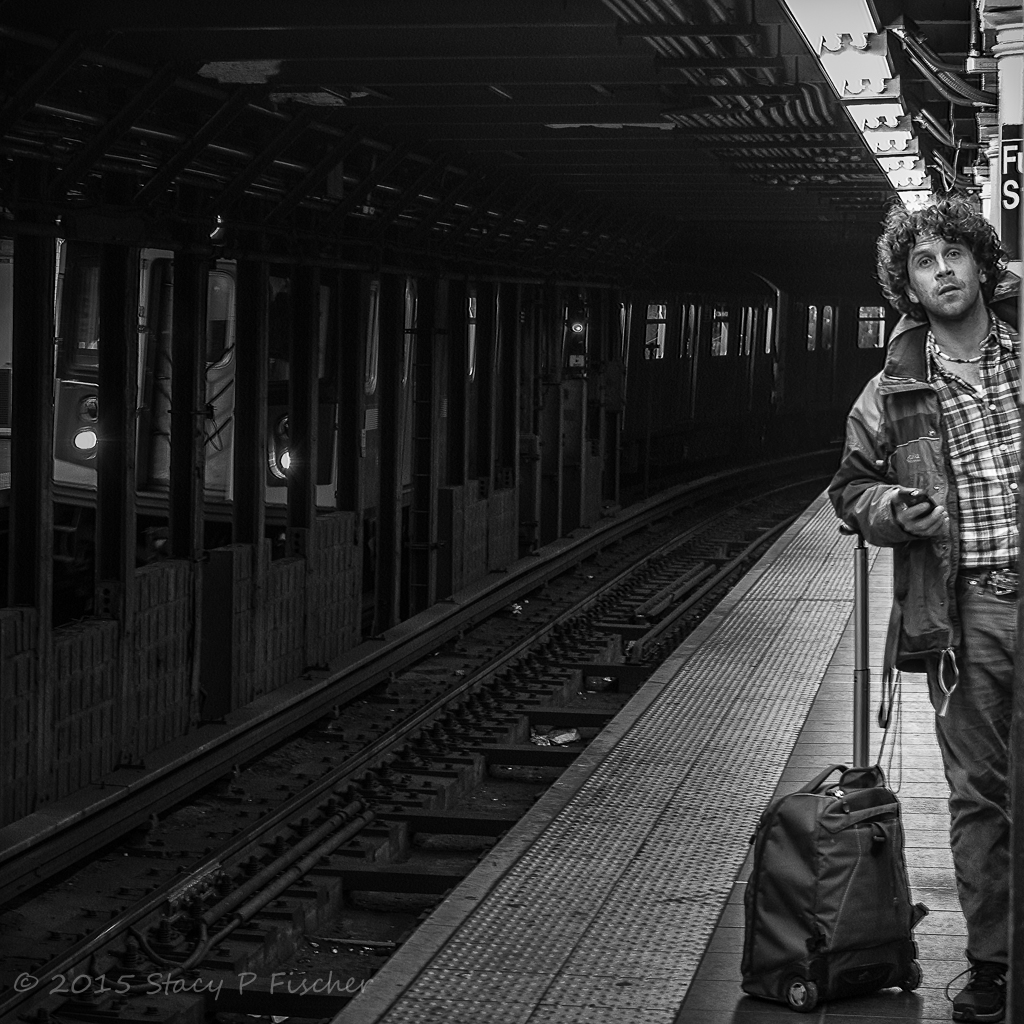 Man peering down New York City subway tracks, waiting for next train.