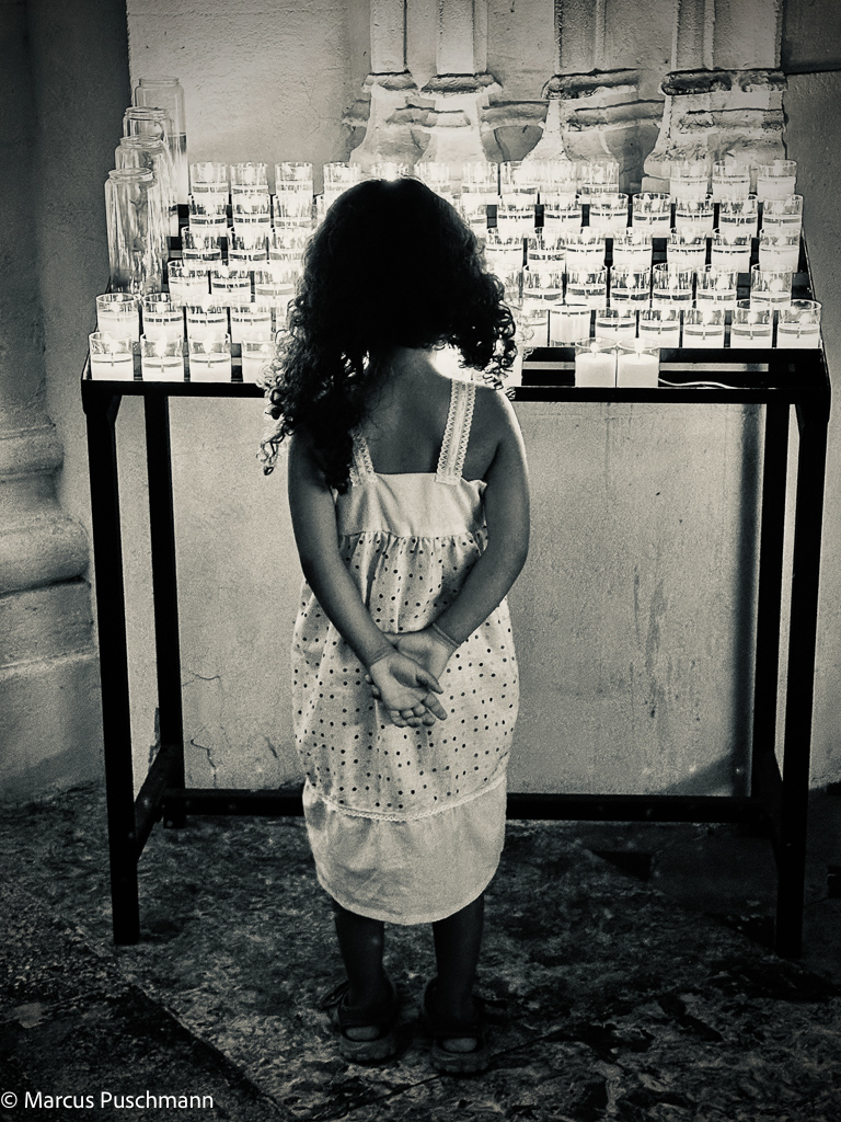 Little girl looking at candles in a church, asking herself which wishes haven been asked for when lighting the candles. 